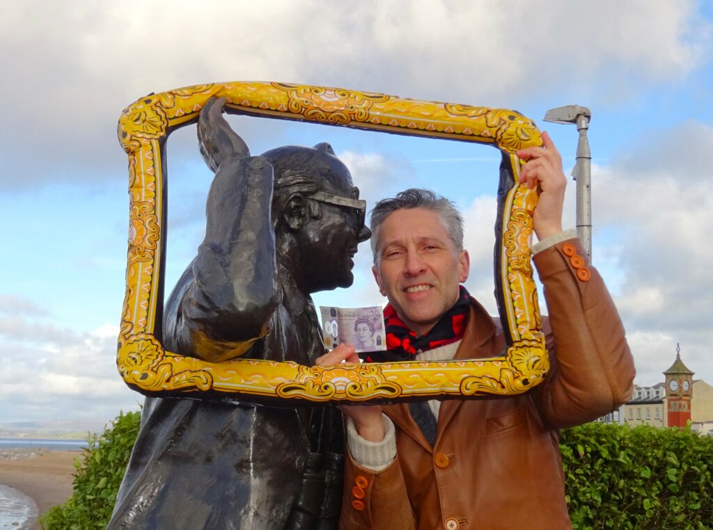 Art Fair/People's Biennial founder Anthony Padgett poses with the Eric Morecambe statue, holding an inflatable picture frame around them both and a £20 note.